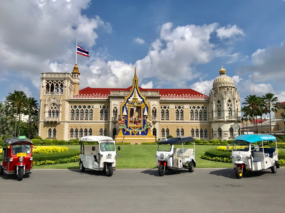Front view of the Government House of Thailand, showcasing Thai Electric Tuk Tuk vehicles, manufactured in Thailand.