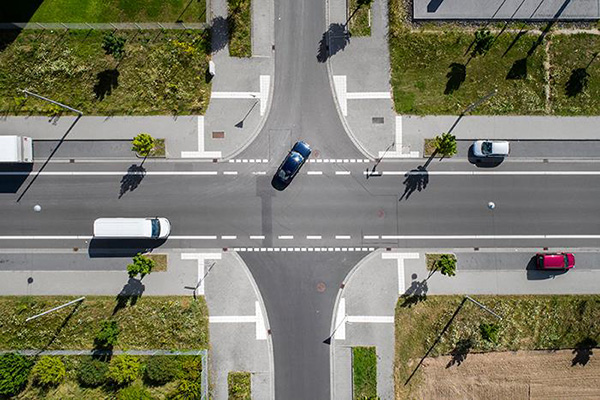 Aerial view of 4 way intersection with parked cars and vehicles driving through.